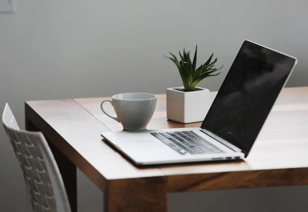 Une table de cuisine avec un portable ouvert sur un appel visio, un carnet et le bol du petit-déjeuner